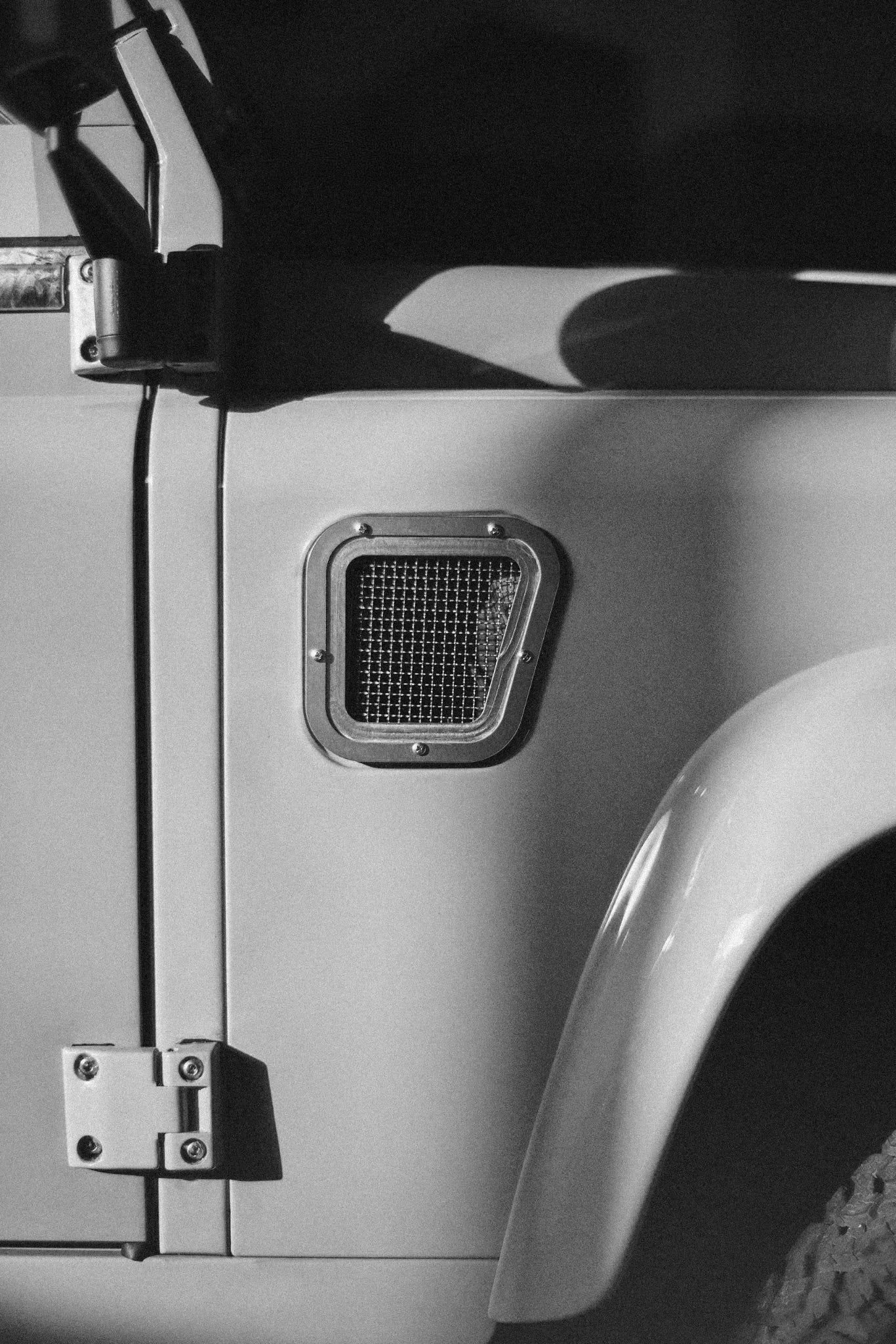 Black-and-white detail of a Defender side vent, bright metal surround and door hinge