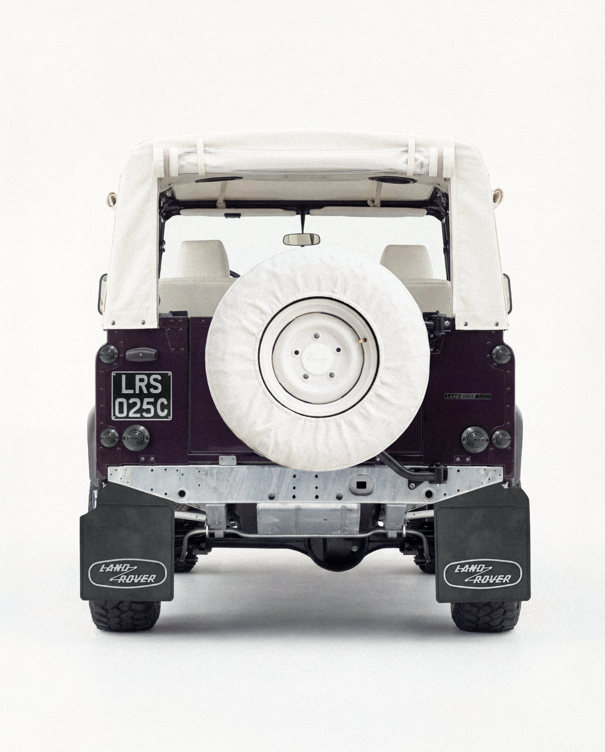 Rear view of an aubergine Defender 90 with a folded soft top and white spare-wheel cover