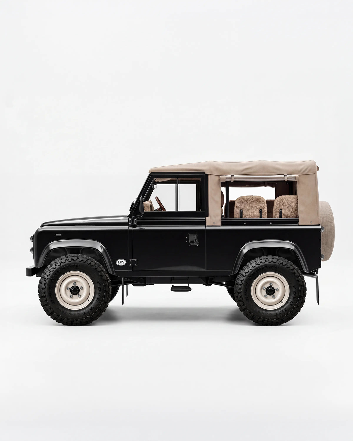 Side profile of a black Defender 90 with a tan canvas soft top