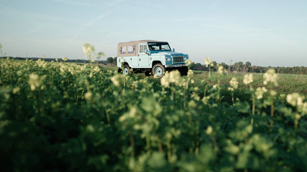 Miami Blue Defender 110 with its canvas soft top in an open field